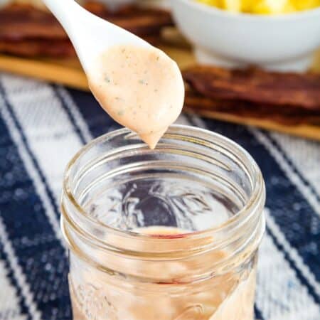 BBQ ranch dressing drops off a spoon into a jar.