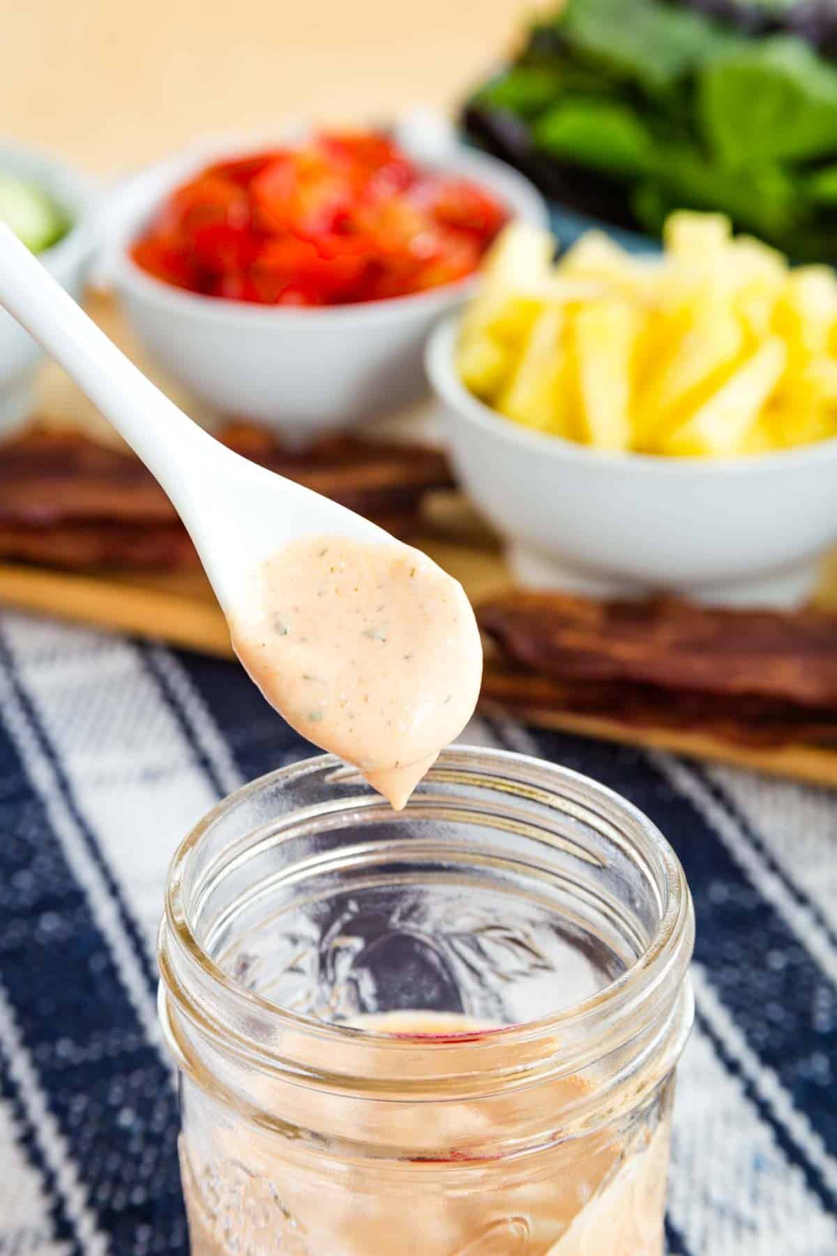 BBQ ranch dressing drops off a spoon into a jar.