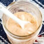A white spoon dips into a jar of BBQ ranch dressing.
