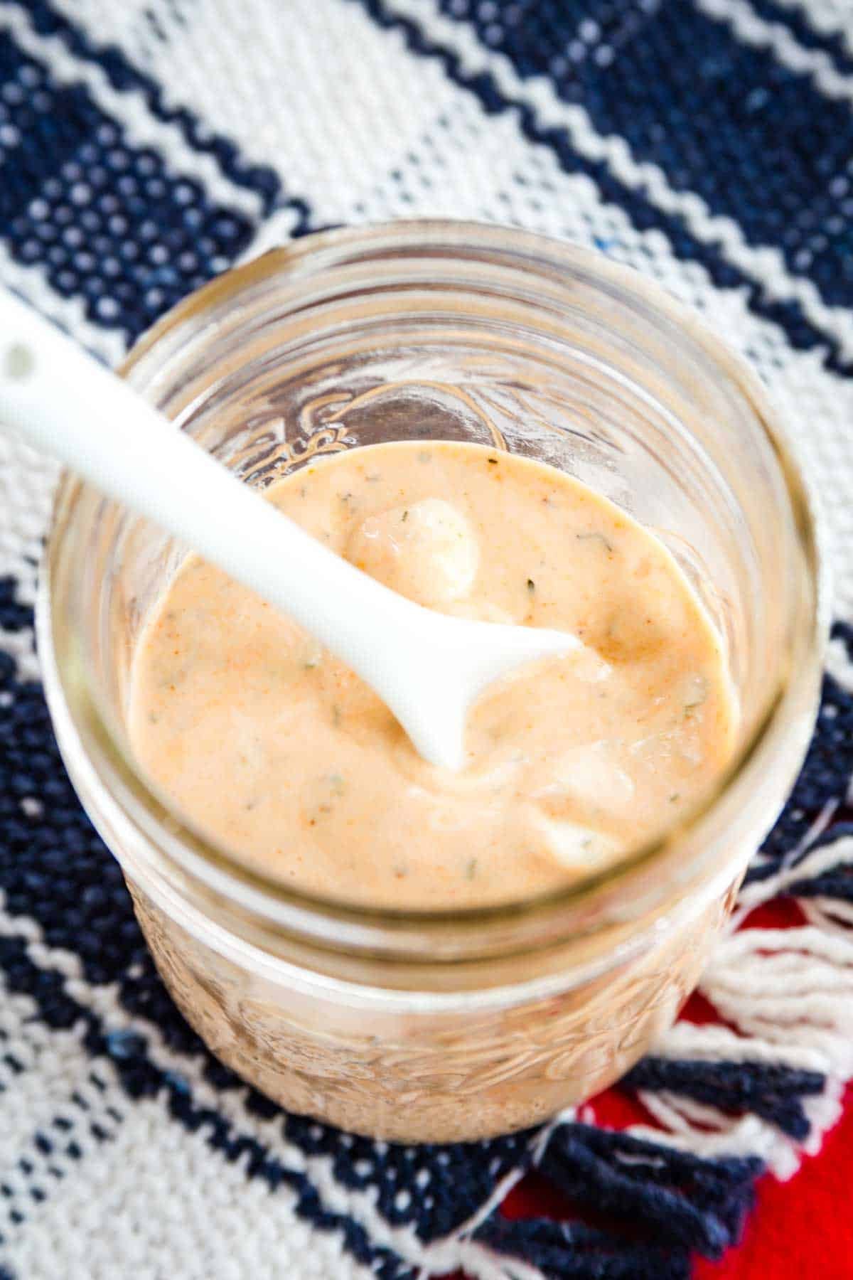 Creamy BBQ ranch dressing is great on salads or as a dip. It's a wonderfully tangy-sweet blend of Greek yogurt, BBQ sauce, and herbs. A white spoon dips into a jar of BBQ ranch dressing.