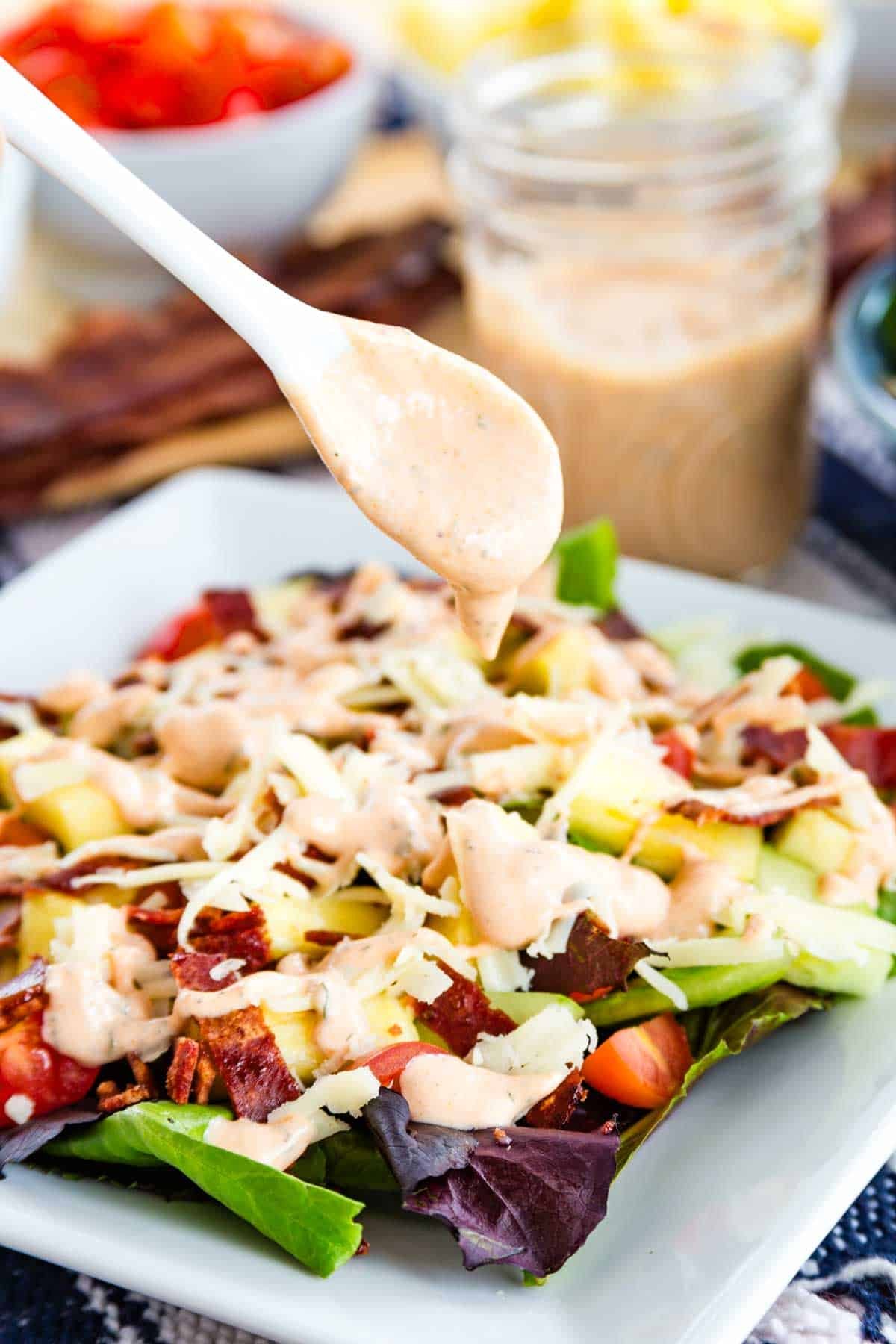 BBQ ranch dressing is drizzled from a spoon onto a salad.