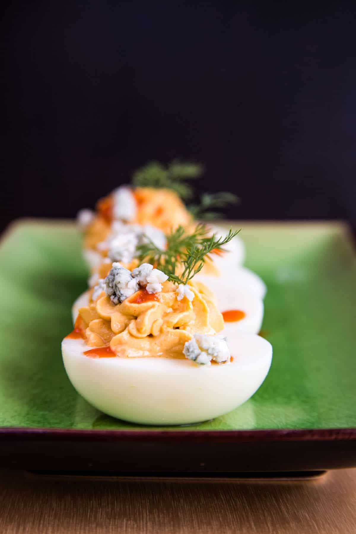 Looking head on at a row of buffalo deviled eggs with blue cheese crumbled on top on a rectangular platter.