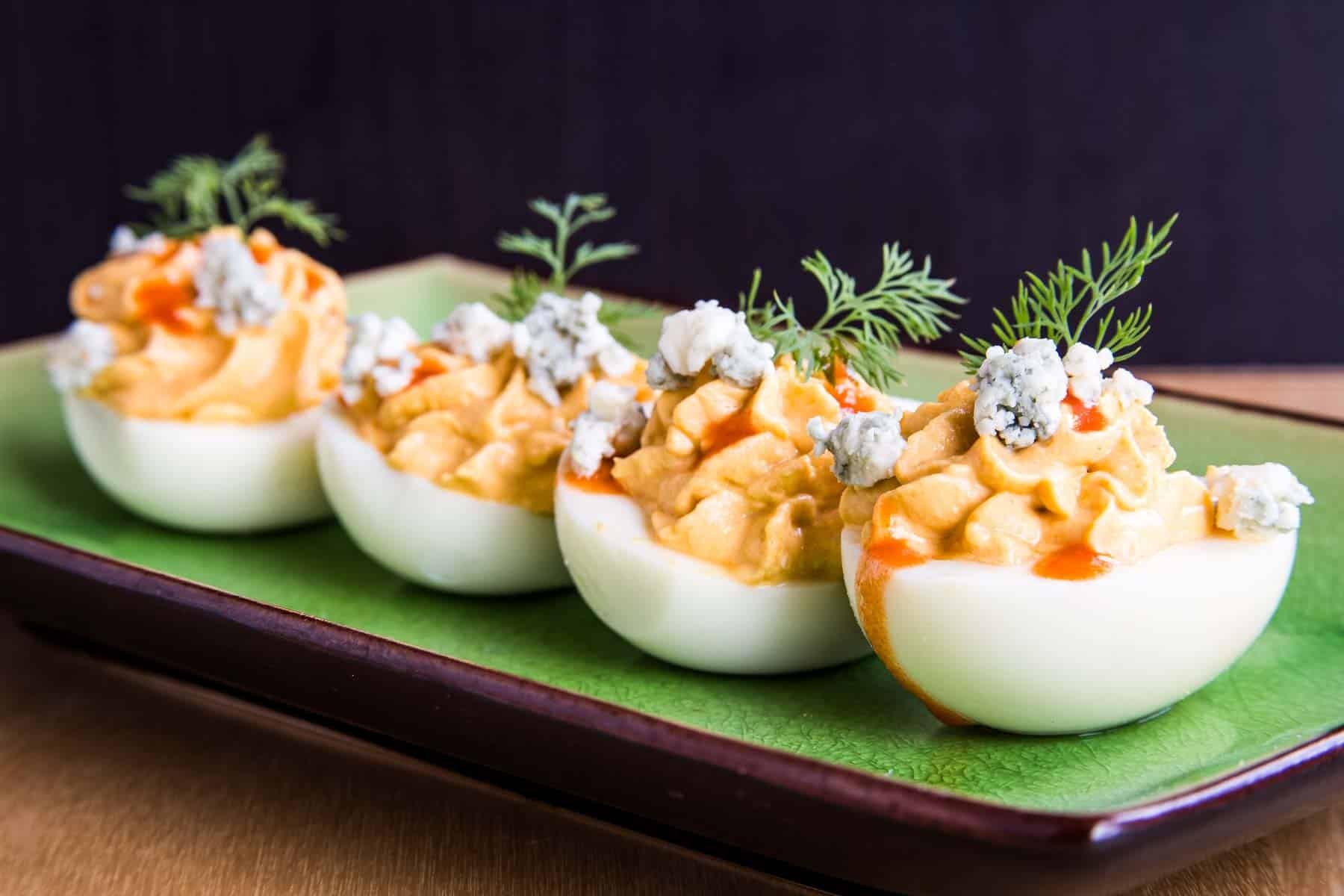 Buffalo deviled eggs garnished with blue cheese and dill on a green plate.