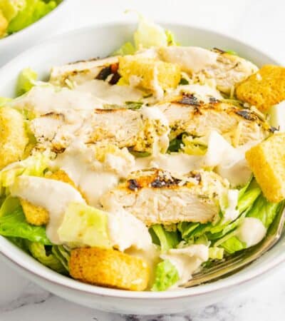 Dressing is drizzled over a bowl of chicken caesar salad.