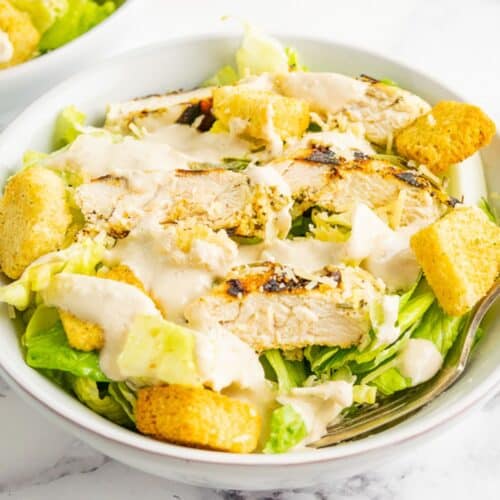 Dressing is drizzled over a bowl of chicken caesar salad.