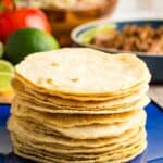 A stack of tortillas on a blue plate with text overlay that says "Homemade Corn Tortillas".