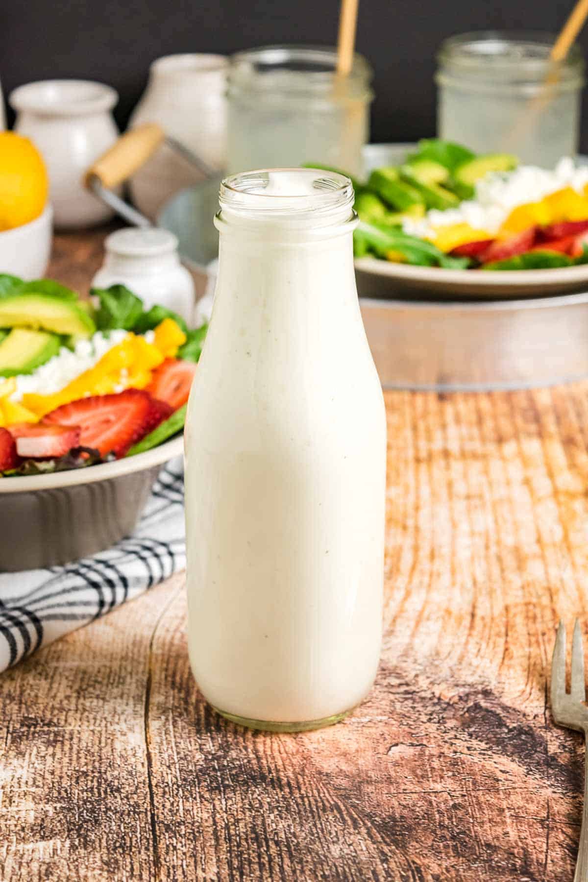 Liven up your favorite salads with this 5-ingredient creamy citrus dressing! Made with Greek yogurt and fresh fruit juice. A tall bottle of creamy citrus dressing in front of fresh vegetables.