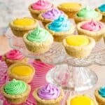 Cookie cups filled with colorful frosting and lemon curd on a glass tiered cake plate with text overlay that says "Gluten Free Sugar Cookie Cups".