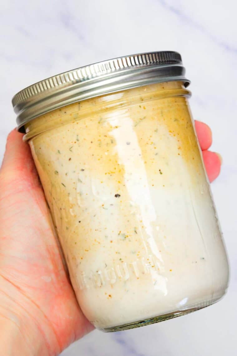 A hand shakes up a jar of BBQ ranch dressing.