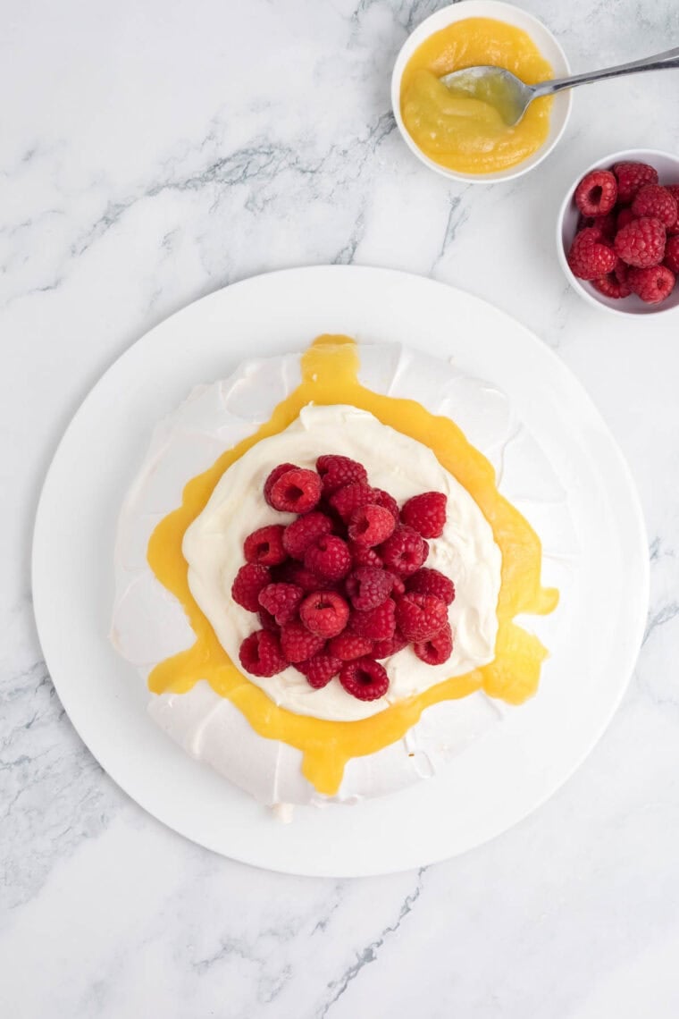 Raspberries are added to the top of a pavlova.