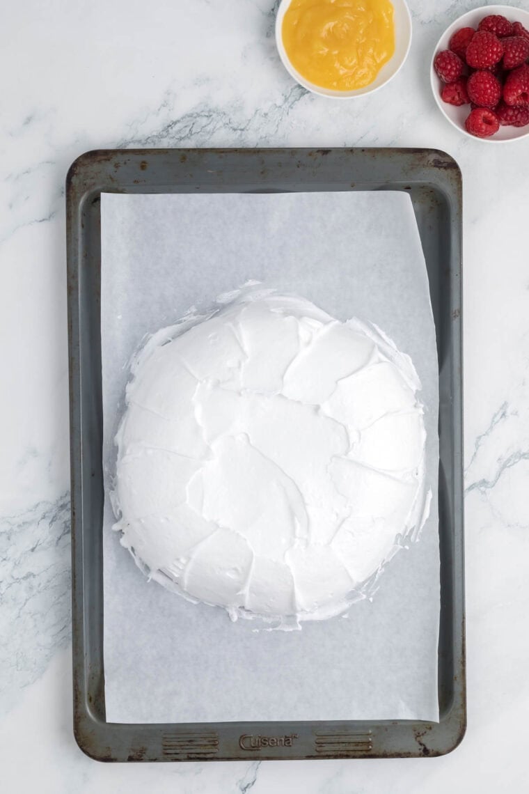 A pavlova cools on a baking sheet lined with parchment paper.