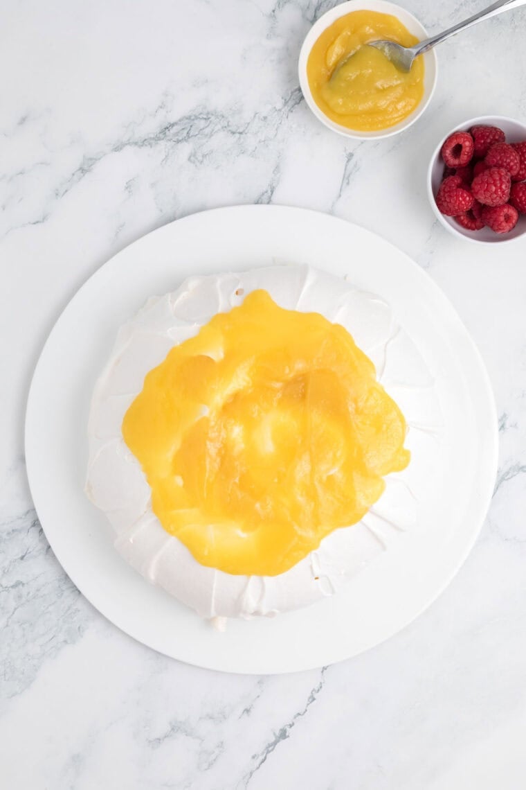 Lemon curd is spread in the center of the top of a pavlova.