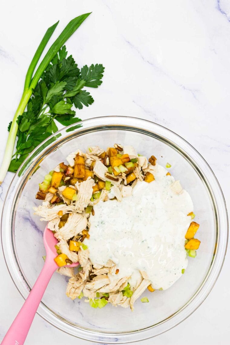 Dressing is added to a bowl of pecan chicken salad.