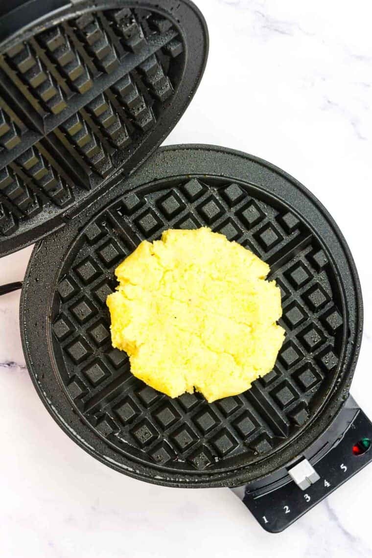 Cheesy polenta waffles batter in a waffle iron.