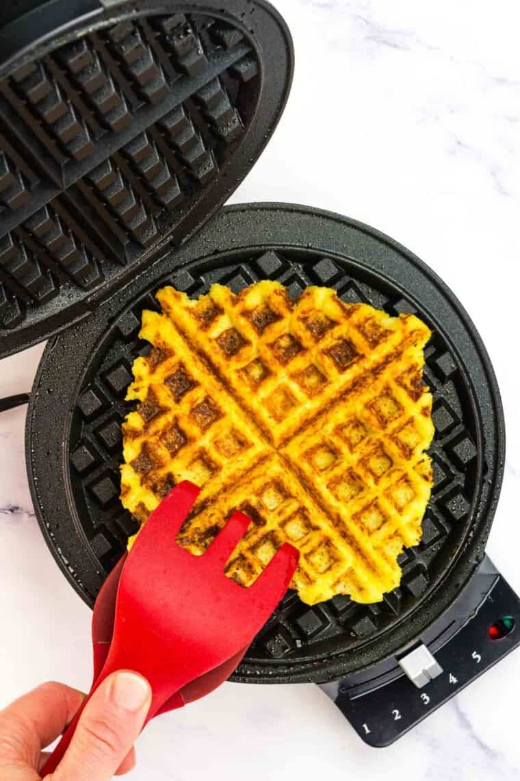 A large fork presses into a polenta waffle in a waffle iron.