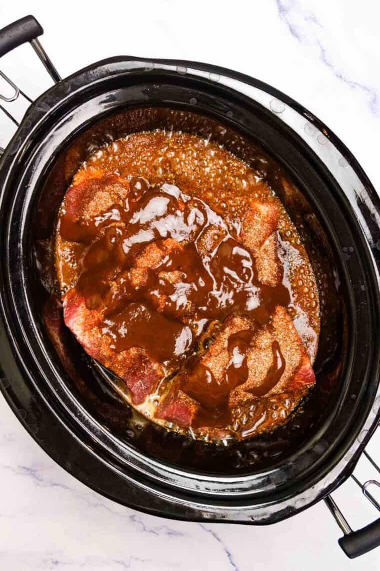 Pork is topped with BBQ sauce in a slow cooker.