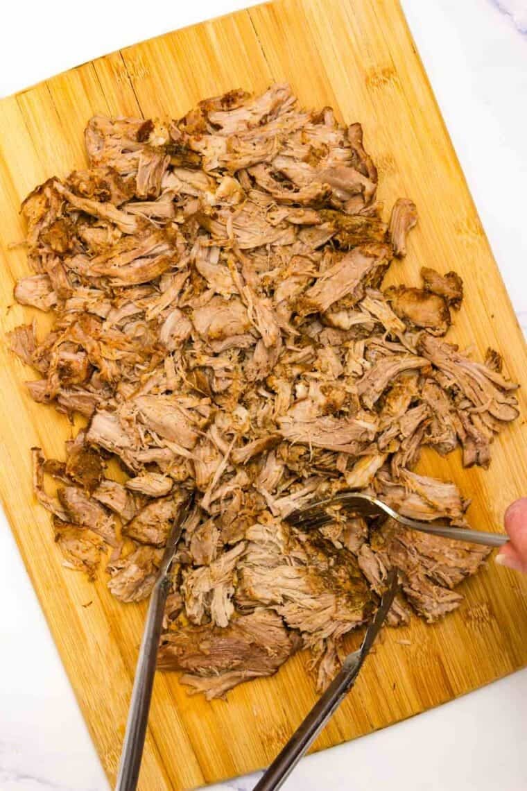 Cooked pork is shredded on a cutting board.