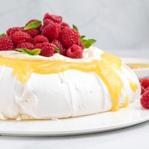 A pavlova is topped with lemon curd, whipped cream, fresh raspberries, and mint.