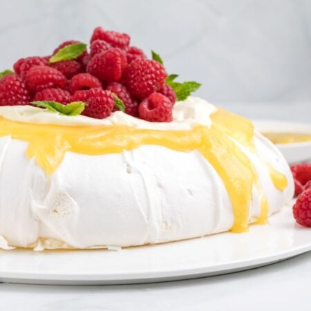 A pavlova is topped with lemon curd, whipped cream, fresh raspberries, and mint.