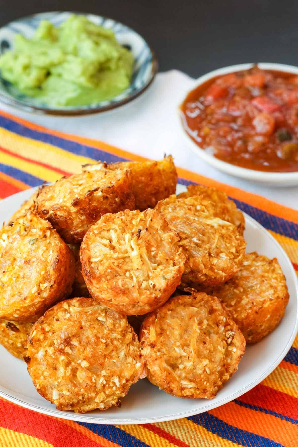 A plate of spicy cauliflower tots on a striped napkin with small dishes of salsa and guacamole in the background.