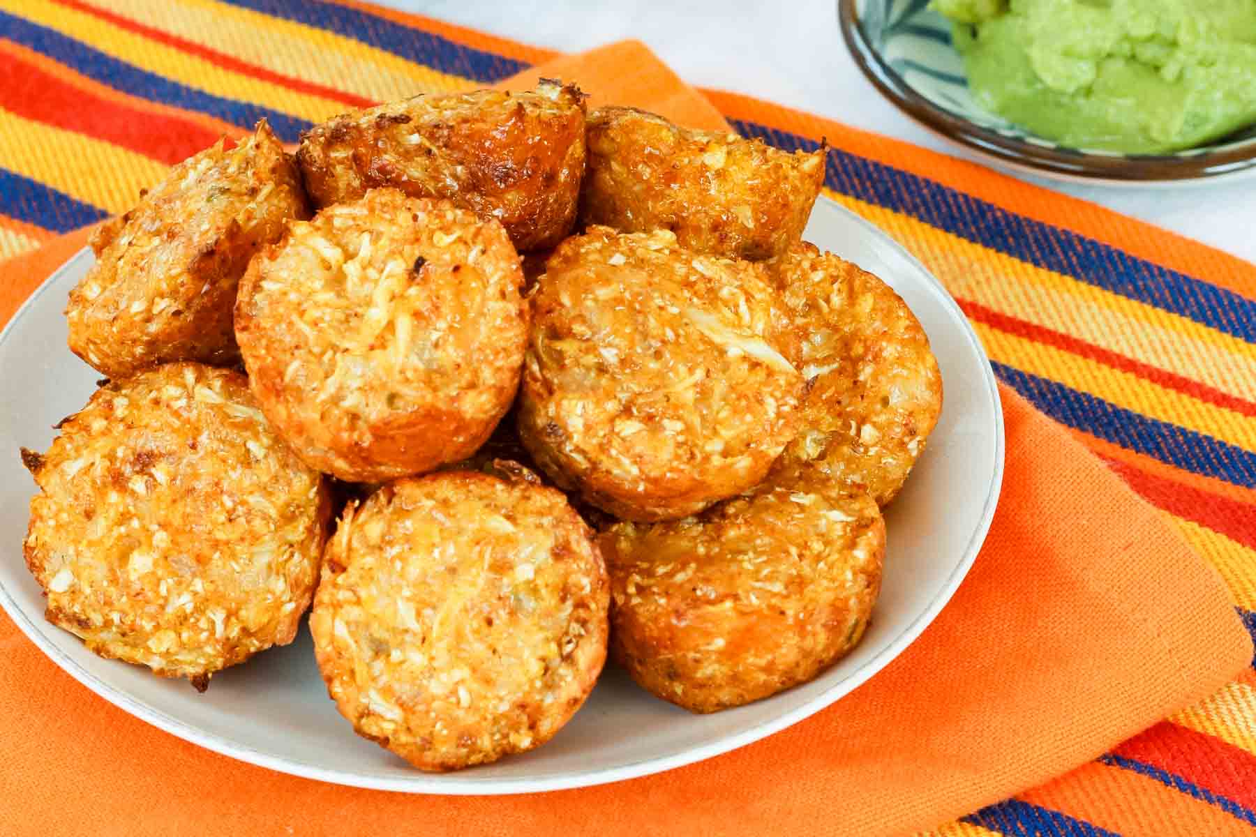 A pile of Mexican Cauliflower Tots on a small white plate on an orange napkin with a striped one beneath it.