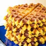 Cheesy polenta waffles are stacked up on a plate.