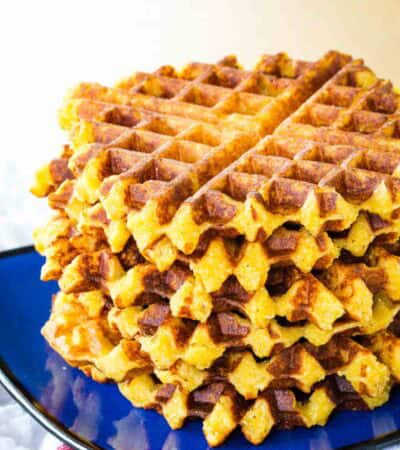 Cheesy polenta waffles are stacked up on a plate.