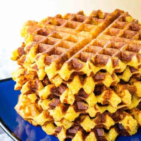 Cheesy polenta waffles are stacked up on a plate.