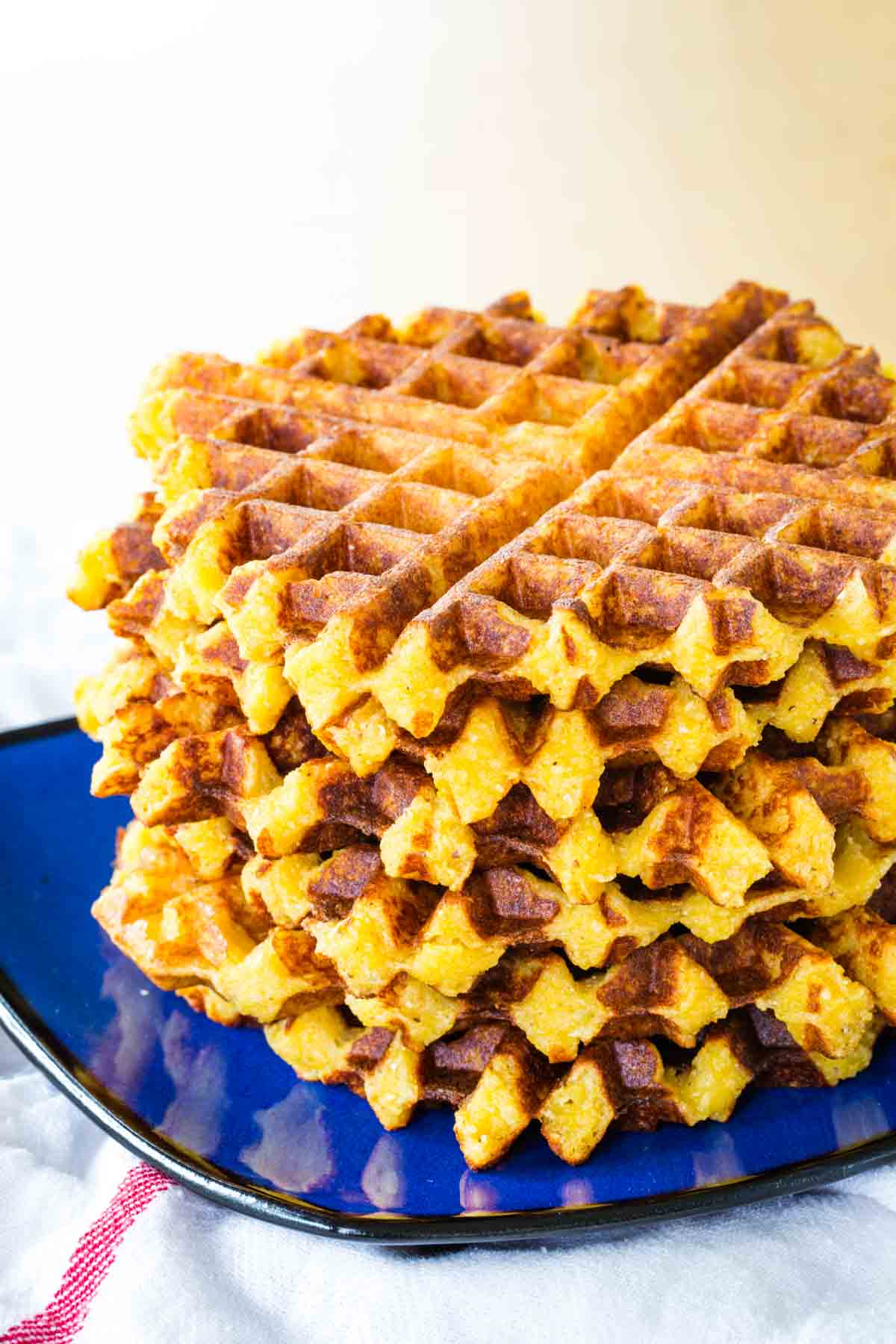 Cheesy polenta waffles trade flour for polenta to make an easy comfort food side dish! Great served any time of the day. Cheesy polenta waffles are stacked up on a plate.