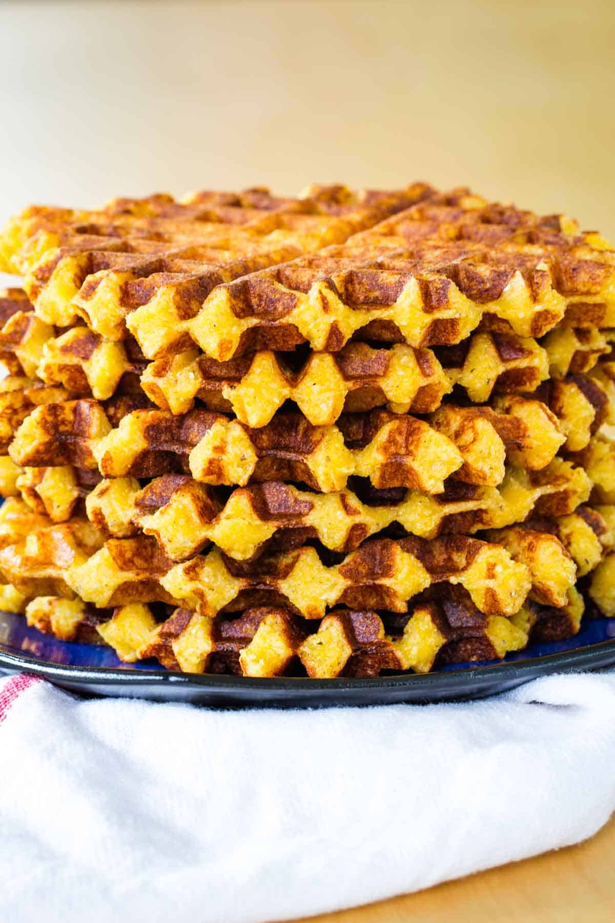 Six cheesy polenta waffles are stacked on top of each other.