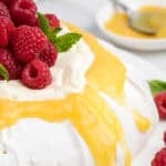 Lemon curd drips down the sides of a pavlova that's also topped with whipped cream and raspberries.