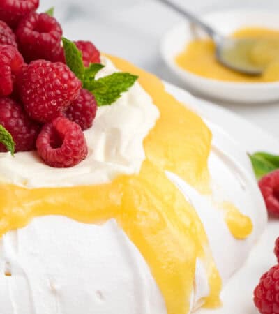 Lemon curd drips down the sides of a pavlova that's also topped with whipped cream and raspberries.