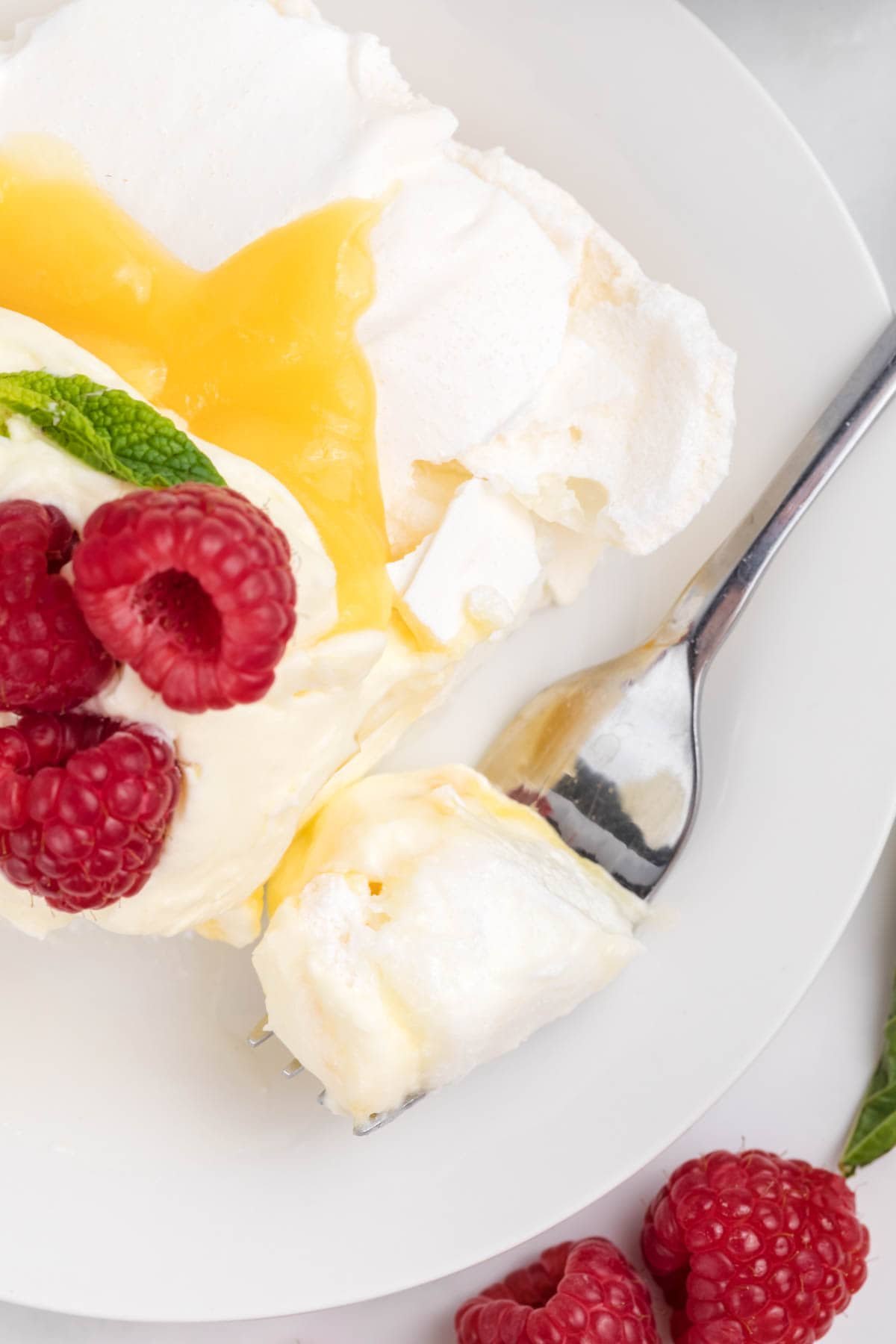 A fork holds a bite of pavlova on a plate.