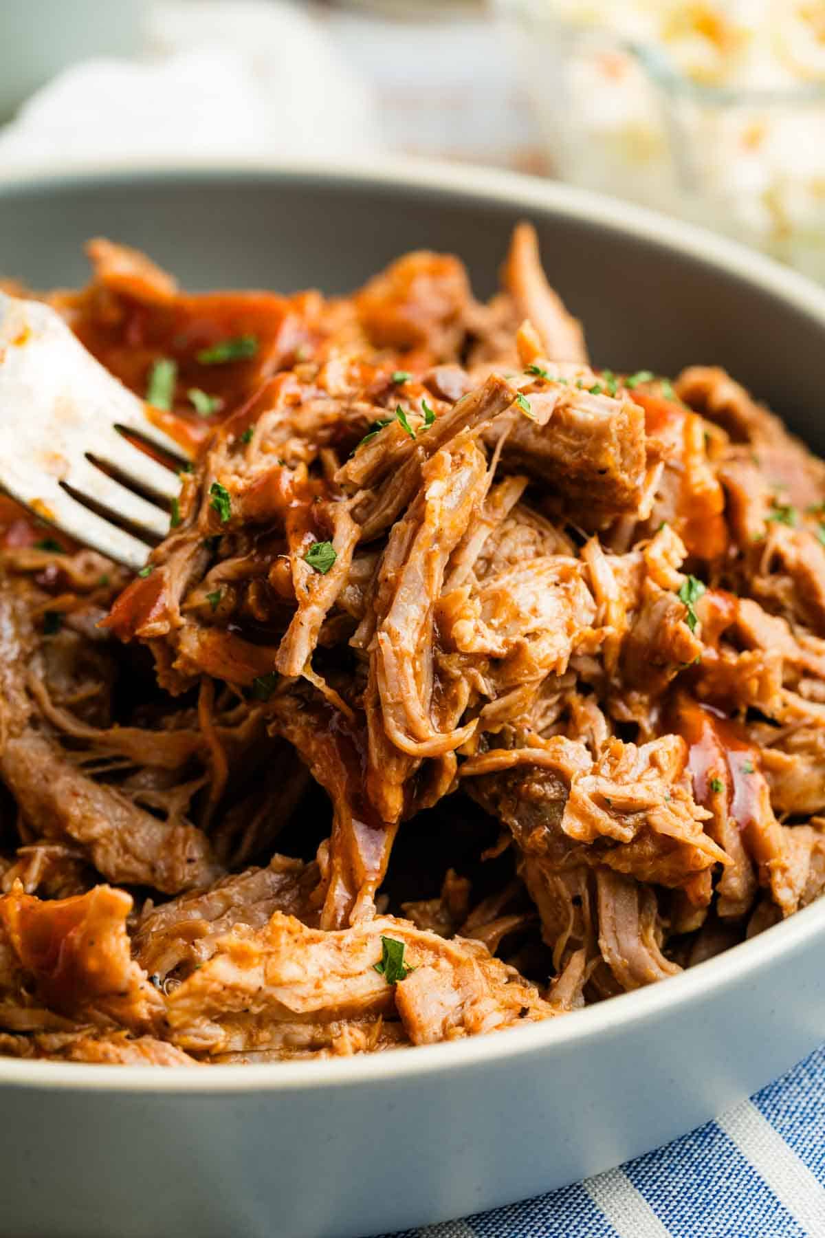 All you need for this easy slow cooker pulled pork recipe is root beer, your favorite barbecue sauce, and a slow cooker. A fork digs into a bowl of slow cooker pulled pork.