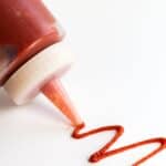 A squiggle of spicy ketchup next to a bottle of ketchup.