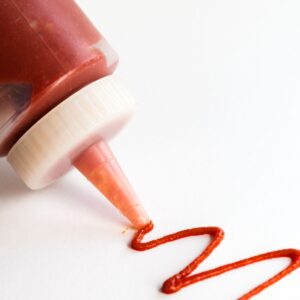 A squiggle of spicy ketchup next to a bottle of ketchup.