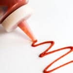 A bottle of spicy ketchup squeezes out a little ketchup.