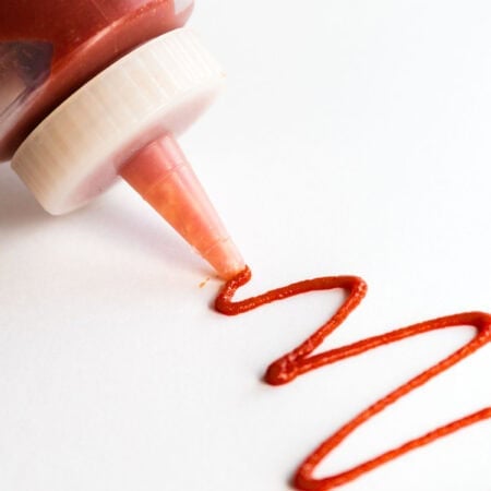 A bottle of spicy ketchup squeezes out a little ketchup.