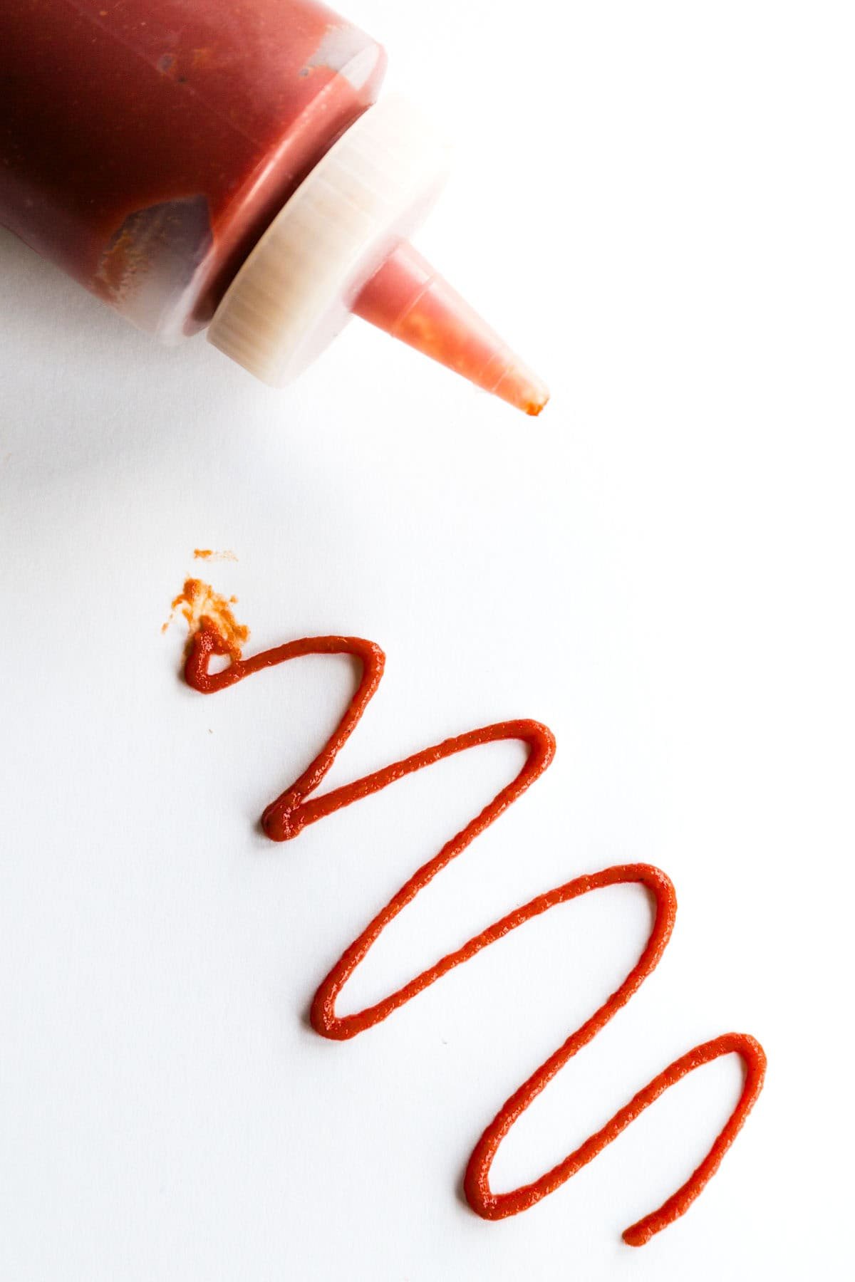 This spicy ketchup recipe makes the best homemade ketchup in just 5 minutes with a hot sauce for a kick of heat. Great on burgers! A squiggle of spicy ketchup next to a bottle of ketchup.