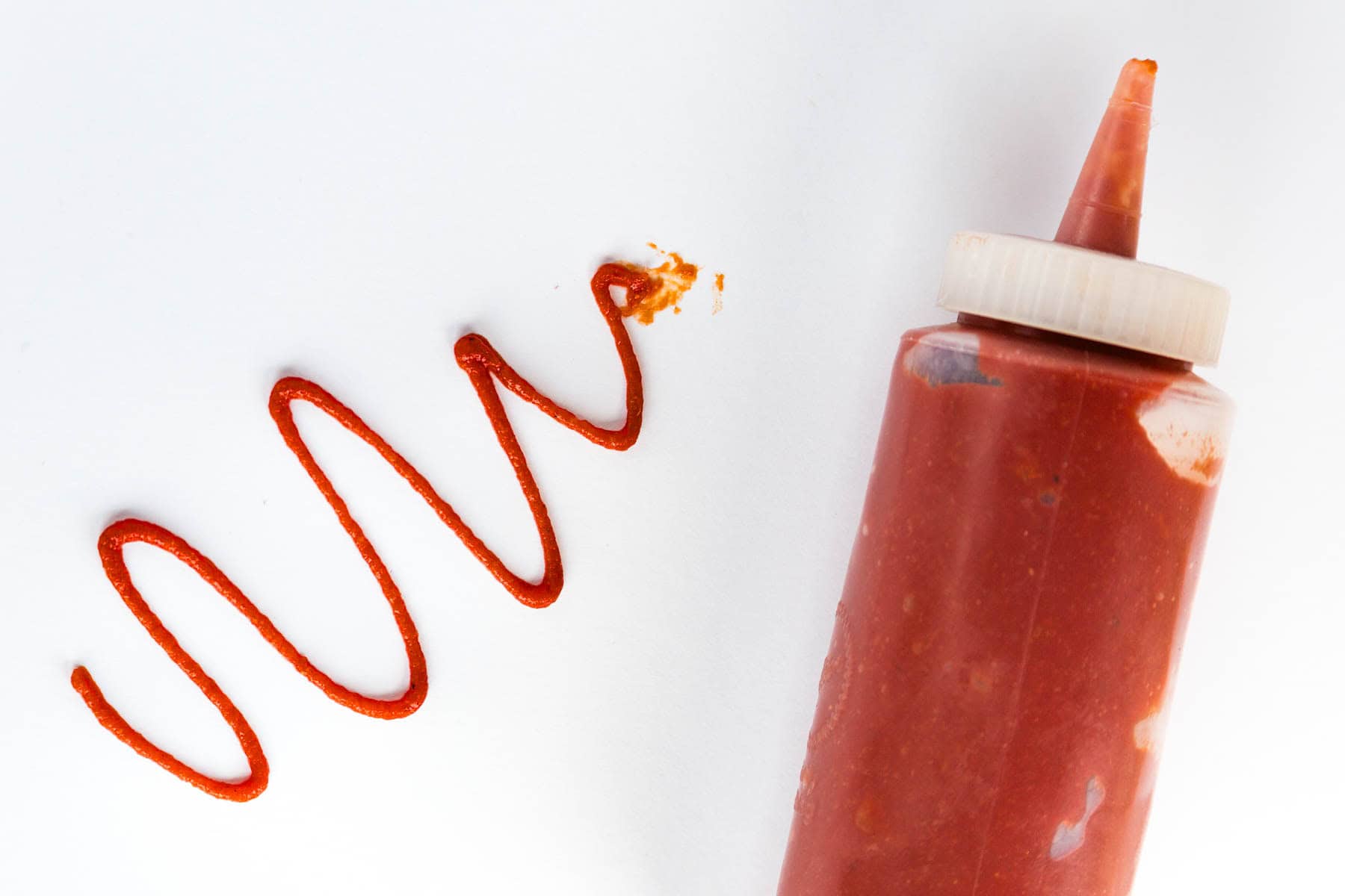 A squiggle of spicy ketchup next to a bottle of ketchup.