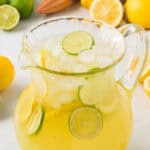A glass pitcher full of lemon limeade and lemon and lime slices.
