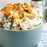 Ranch potato salad topped with bacon is served in a grey bowl.