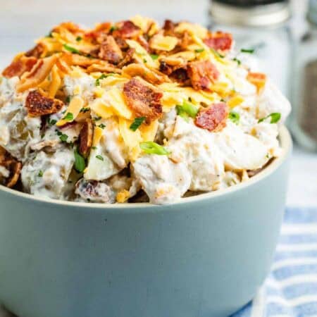 Ranch potato salad topped with bacon is served in a grey bowl.