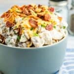 A bowl of potato salad topped with crumbled bacon and shredded cheddar cheese with text overlay that says "Bacon Ranch Potato Salad".