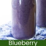 A purple-colored smoothie in a glass bottle and looking down into the bottle with small wild blueberries floating on top divided by a green box with text overlay that says "Blueberry Smoothie" and the words "Get the Recipe!".