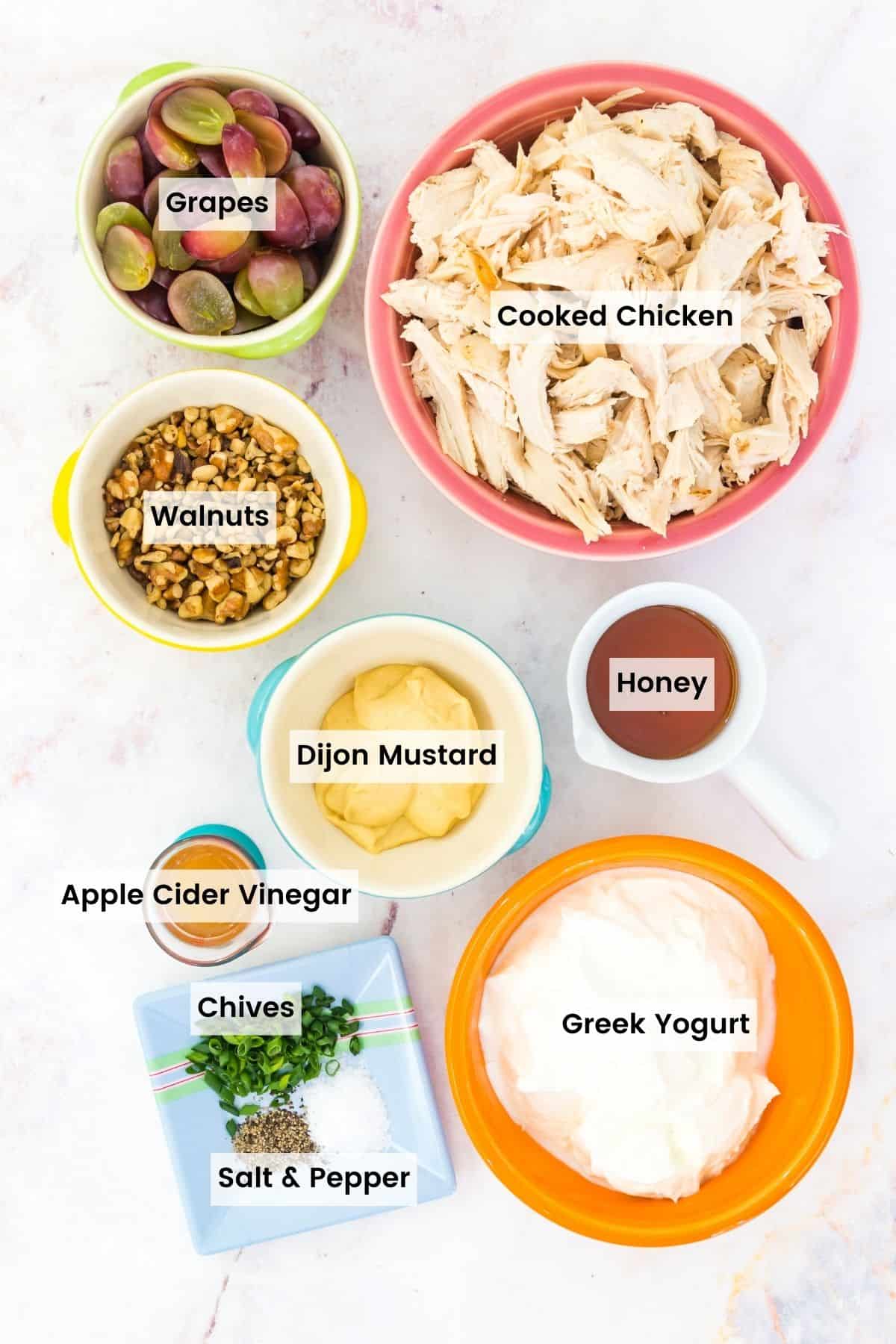 Bowls of chicken salad ingredients on a marble countertop with text labels.