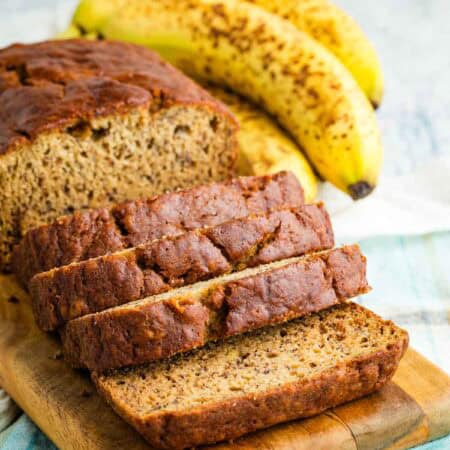 A loaf of gluten-free banana bread cut into slices on a cutting board.