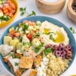 A Greek chicken bowl surrounded by some of the ingredients that went into it.