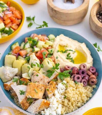 A Greek chicken bowl surrounded by some of the ingredients that went into it.