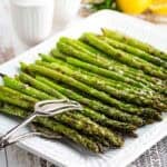 A square plate of grilled asparagus with serving tongs/